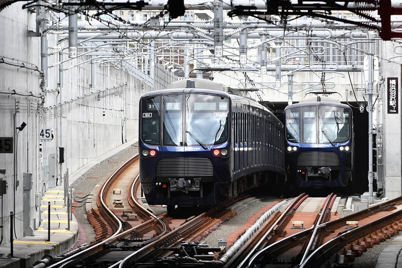 線路の分岐器の奥に、紺色の車両2編成が並走して正面から近づいてくる、イメージ